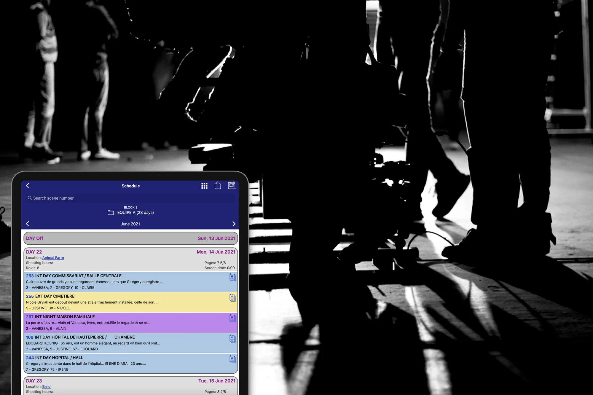 A tablet showing the app's shooting schedule — colour-coded scenes across June dates with locations and cast — held against a black-and-white film set where a crew works behind a camera.