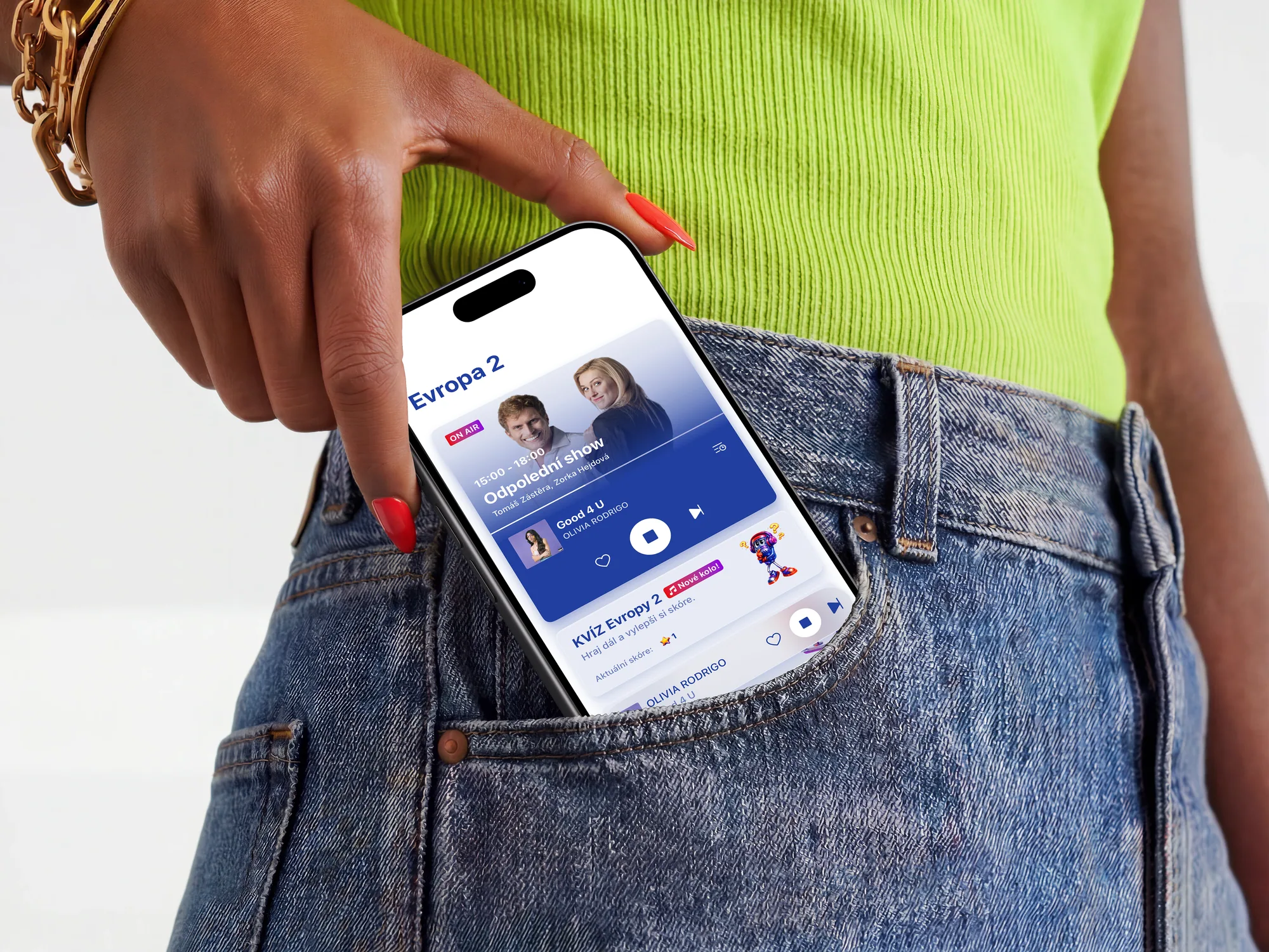 A phone being lifted from the back pocket of a pair of jeans, its screen showing the Evropa 2 app mid-broadcast: the afternoon show on air above the track playing now.